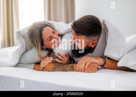 Young happy loving couple is lying in bed in the morning. They are embracing. Stock Photo