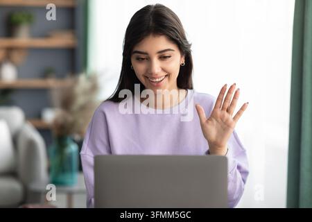 Modern Remote Communication Concept. Headshot portrait of cheerful young woman making online video call using laptop and waving to webcam, casual lady Stock Photo
