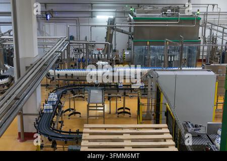 Automated milk bottling line with white bottles on stainless steel conveyors inside a modern dairy factory. Stock Photo