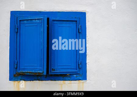 Blue window shutter slightly open on a white wall Stock Photo
