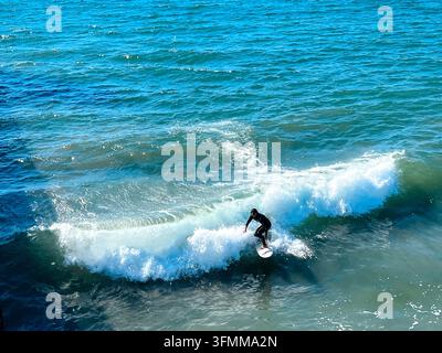 Aerial view of a surfer riding a breaking wave, white water spray trailing behind against vivid turquoise ocean, Ocean Beach, San Diego, California Stock Photo