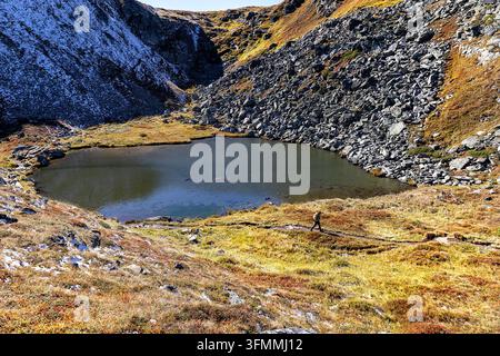 A tourist hiker with a backpack trekking along a scenic gravel path through alpine meadows on the spectacular Kaltenbachsee tour, Austria. Stock Photo