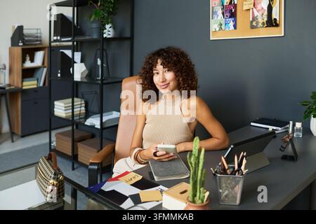 Portrait of Biracial Woman Brand Designer Using Smartphone at Desk Stock Photo