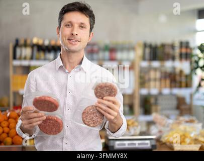 Adult man buyer chooses packaged raw hamburger patty in grocery store Stock Photo