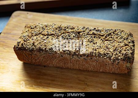 Rectangular multigrain loaf covered with mixed seeds, resting on a wooden cutting board. Stock Photo