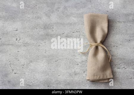 Top view of folded linen napkin tied with rope on gray textured stone surface. Minimal rustic table setting for food styling, eco-friendly design, or Stock Photo