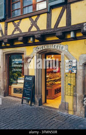 Entrance area of a biscuiterie in a traditional Alsatian half-timbered building, yellow facade with wooden beams, decorative signs on the shop front Stock Photo