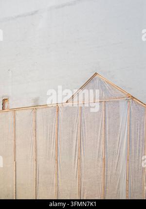 Eine provisorische Holzkonstruktion mit durchscheinender Verkleidung steht unmittelbar vor einer hell verputzten Gebäudewand. Die transparente Abdeckung lässt die darunterliegende Struktur teilweise sichtbar und erzeugt ein grafisches Zusammenspiel aus Linien, Flächen und Licht. *** A temporary wooden structure with a translucent covering stands directly in front of a light-rendered building wall. The transparent covering partially reveals the structure underneath, creating a graphic interplay of lines, surfaces and light. Österreich, Austria 20260928-DSCF7779 Stock Photo
