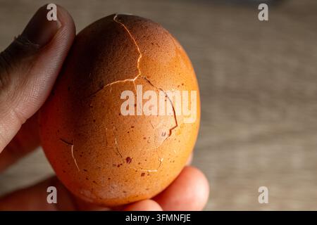 Close-up of a brown chicken egg with a cracked shell held in a human hand, showing damage and fractures on the eggshell Stock Photo