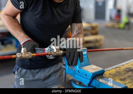Close-up of an industrial worker using an adjustable wrench on a metal pipe fitting in a workshop. Stock Photo