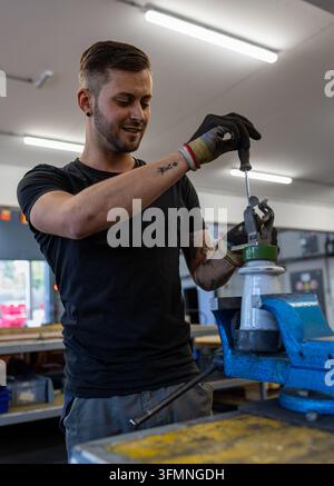 Industrial worker using a screwdriver while repairing a mechanical component in a workshop. Stock Photo