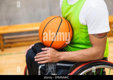 Athlete holding basketball while sitting in wheelchair on court Stock Photo