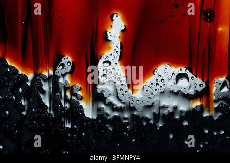 Water droplets and oil combining on a surface, forming an abstract pattern with vibrant red and dark black colors Stock Photo