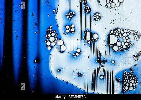 Oil drops merging in water, forming abstract patterns with blue and white liquid bubbles, showcasing a macro fluid art texture Stock Photo