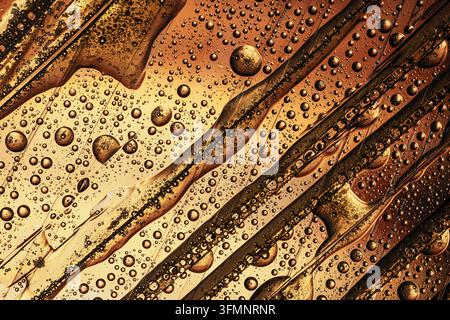 Abstract background showing golden oil and water drops forming unique liquid textures and reflective bubbles on a warm surface Stock Photo