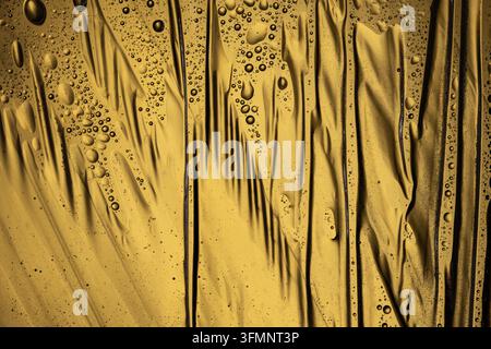 Golden abstract surface with liquid drops and wrinkled plastic texture creating a wet and reflective background Stock Photo