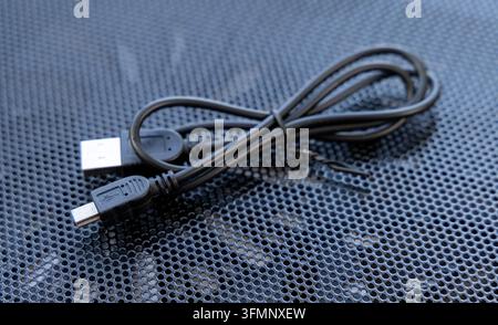 Black charging wire rests on a dark metal mesh surface Stock Photo