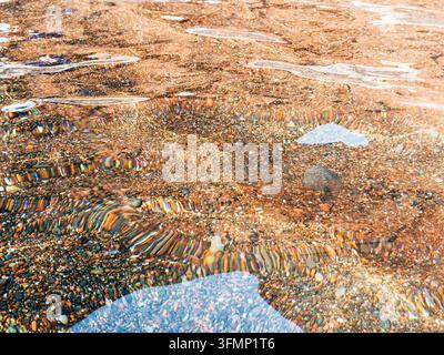 Close-up of sunlight refracting through gentle ripples over colorful pebbles and stones in clear shallow beach water, creating a natural abstract text Stock Photo