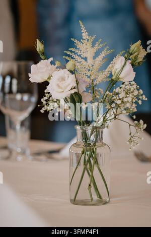 Elegant table decoration featuring white roses in a glass vase against a solid blue background Stock Photo