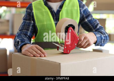 Worker sealing cardboard box with adhesive tape in warehouse, closeup Stock Photo