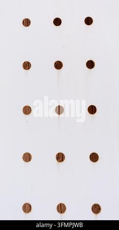 White painted metal panel with rows of round holes and rust streaks, close-up of weathered perforated surface Stock Photo