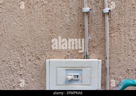 Old surface-mounted toggle switch in the ON position with exposed wiring and conduit on a rough render wall Stock Photo