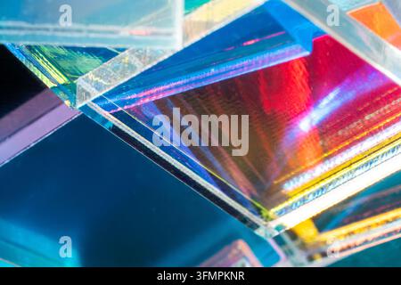 Close-up of overlapping iridescent glass prisms reflecting vivid cyan, magenta, red and yellow light, creating an abstract technological background wi Stock Photo