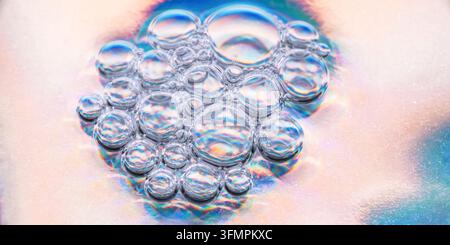 Macro view of a translucent bubble cluster floating in liquid, with iridescent rainbow reflections, soft pastel light, and abstract scientific texture Stock Photo