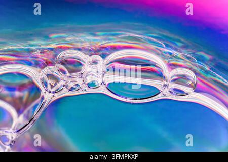 Macro photograph of transparent soap bubbles floating on water, highlighted by vivid blue, pink and purple iridescent reflections in an abstract scien Stock Photo