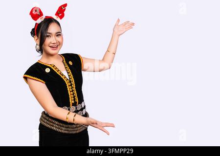 A smiling young Sabahan woman in traditional Kadazan Dusun dress presents toward copy space on the right while wearing red Christmas reindeer antlers. Stock Photo