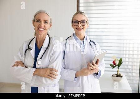 Smiling female doctors wear white coats standing in hospital office Stock Photo