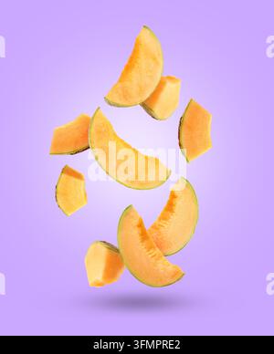 Pieces of cantaloupe melon falling on violet background Stock Photo