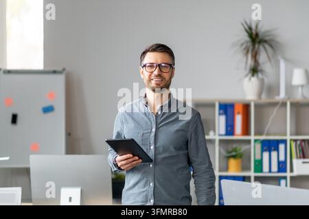 Young Caucasian Man Holding Tablet In Office, Smiling, Business Concept Stock Photo