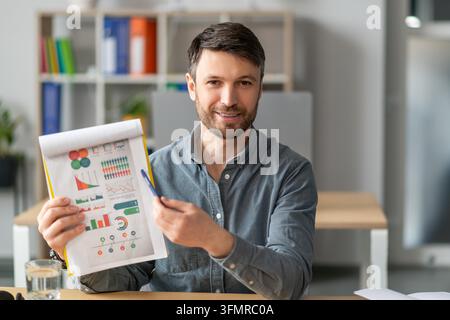 Young Caucasian Man Presenting Business Charts In Office, Engaged And Focused Stock Photo