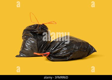 Waste management and environmental pollution, black plastic garbage bags for household trash disposal on a solid yellow background Stock Photo