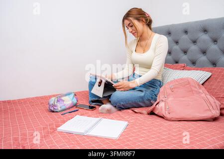 Young woman studying at home in bed, concentrating on digital content with a tablet, embracing comfortable remote e-learning and online education conc Stock Photo