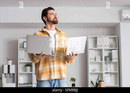 Multitasking and work overload, man holding two laptops in office environment with professional stress and digital burnout Stock Photo