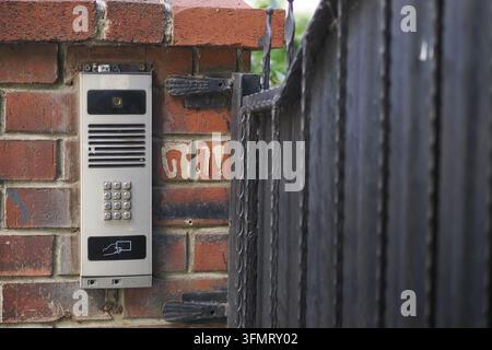 Intercom system mounted on a brick wall near a metal gate Stock Photo