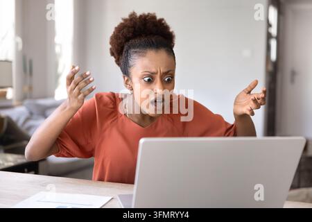 Woman raises hands in disbelief while staring at laptop screen Stock Photo