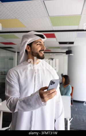 Thoughtful Middle Eastern businessman holding smartphone in office Stock Photo