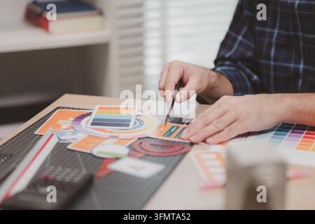 Designer working with color palettes, layout templates, and creative design tools on a desk while planning branding and graphic design projects in a m Stock Photo