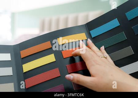 Close-up of a customer selecting colorful upholstery swatches from a fabric sample book in a furniture store, comparing texture and color options for Stock Photo
