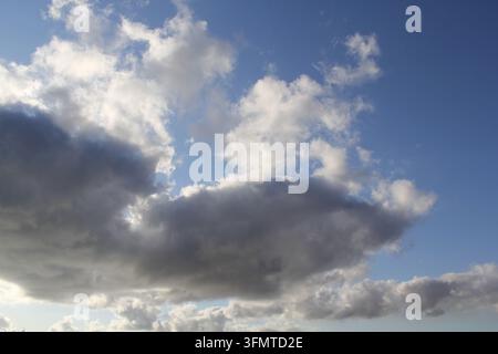 Dark, heavy storm clouds gathering beneath lighter, sunlit cumulus clouds in a blue sky Stock Photo