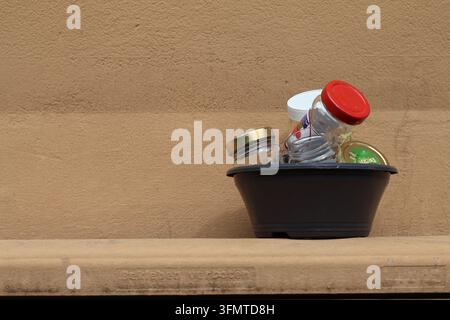 Empty glass jars with colorful lids collected in a plastic bowl for recycling against a beige wall Stock Photo