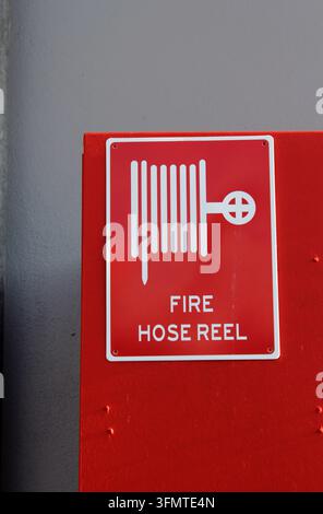 A red "Fire Hose Reel" safety sign with a white hose symbol mounted on a red wall box Stock Photo