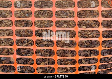 Close-up pattern of bright orange plastic safety mesh fencing overlying brown woodchip mulch Stock Photo