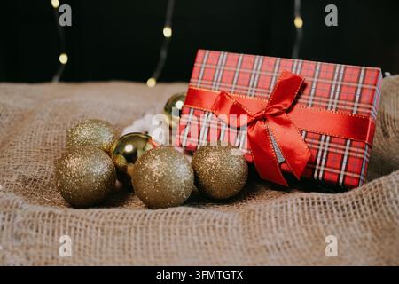 Cozy Christmas arrangement with a red plaid present, ribbon and golden baubles on a textured fabric surface, evoking seasonal warmth, gift giving Stock Photo