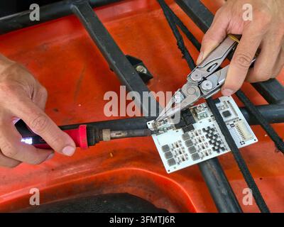 An electronic circuit board repair with soldering iron and precision plier on red work surface Stock Photo
