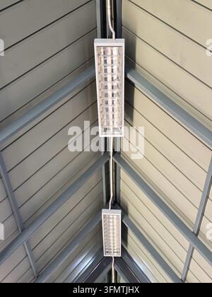 An industrial ceiling light fixture mounted beneath peaked metal roof, creating symmetrical geometric interior with clean architectural lines and brig Stock Photo