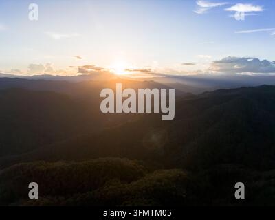A sunset over mountain range and forest valley with golden light, layered ridges, dramatic cloud, and tranquil wilderness landscape creating peaceful Stock Photo
